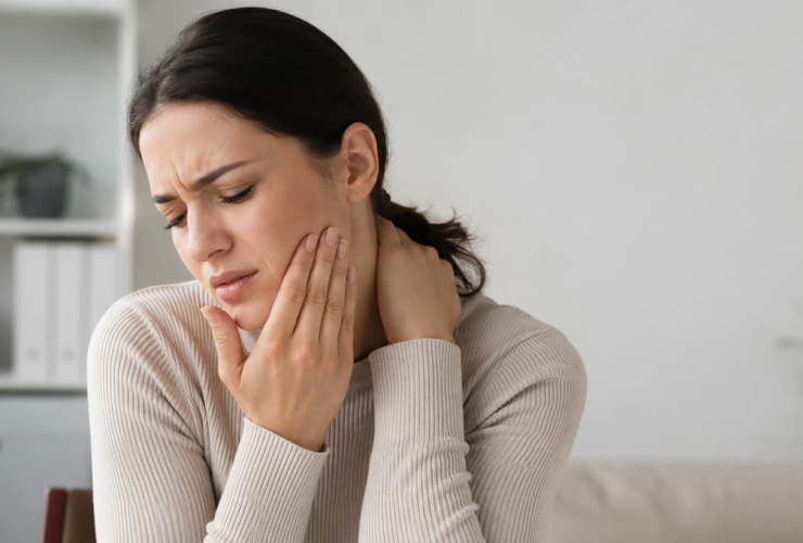 Person holding their jaw and neck with discomfort from possible TMJ-related headache, neck tension, and jaw pain